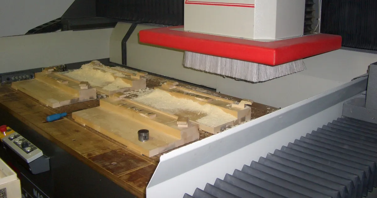 Large CNC gantry machine with a spindle head above a table of wooden workpieces, showing the bridge and bed of a CNC router gantry frame