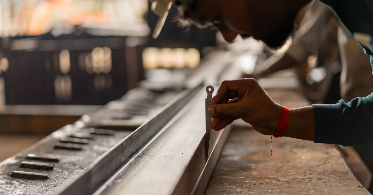 Inspector checking a long steel section with a hand gauge on a workshop bench, the type of check used in frame flatness inspection