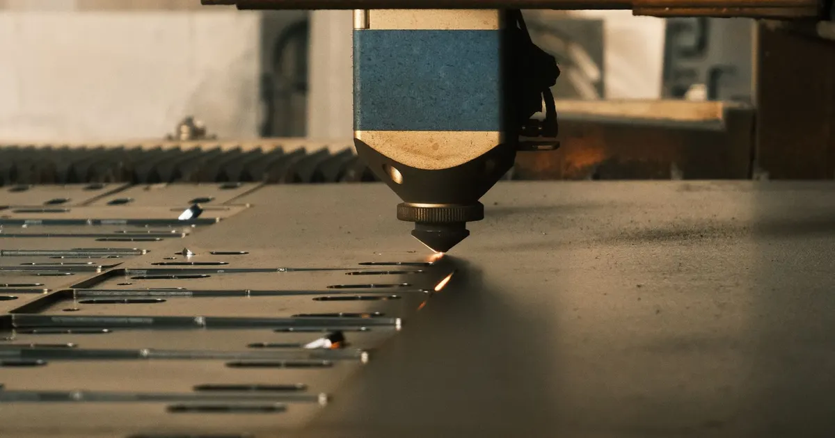 Laser cutting head positioned over a steel sheet with cut parts on a cutting table, showing the bed of a laser cutting machine frame