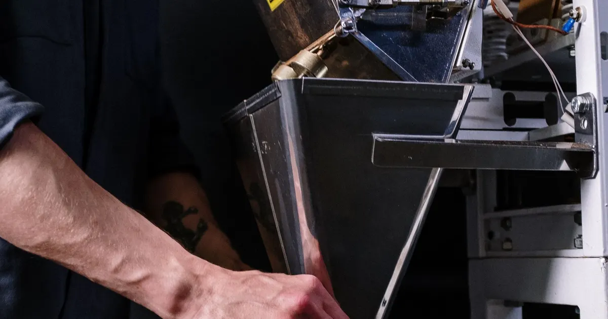 Hand at the stainless steel chute of a packaging machine, showing sheet stainless construction used on packaging machine frames