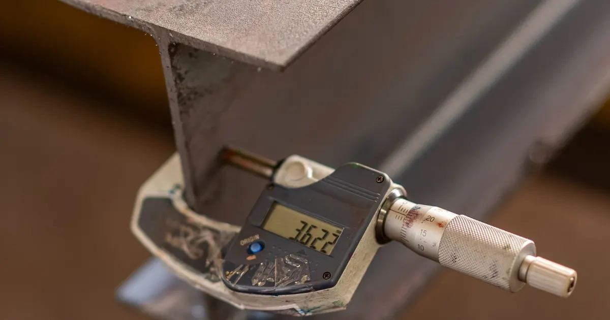 Digital micrometer measuring the thickness of a steel section in a workshop, a check used for plate thickness tolerance on machine frames
