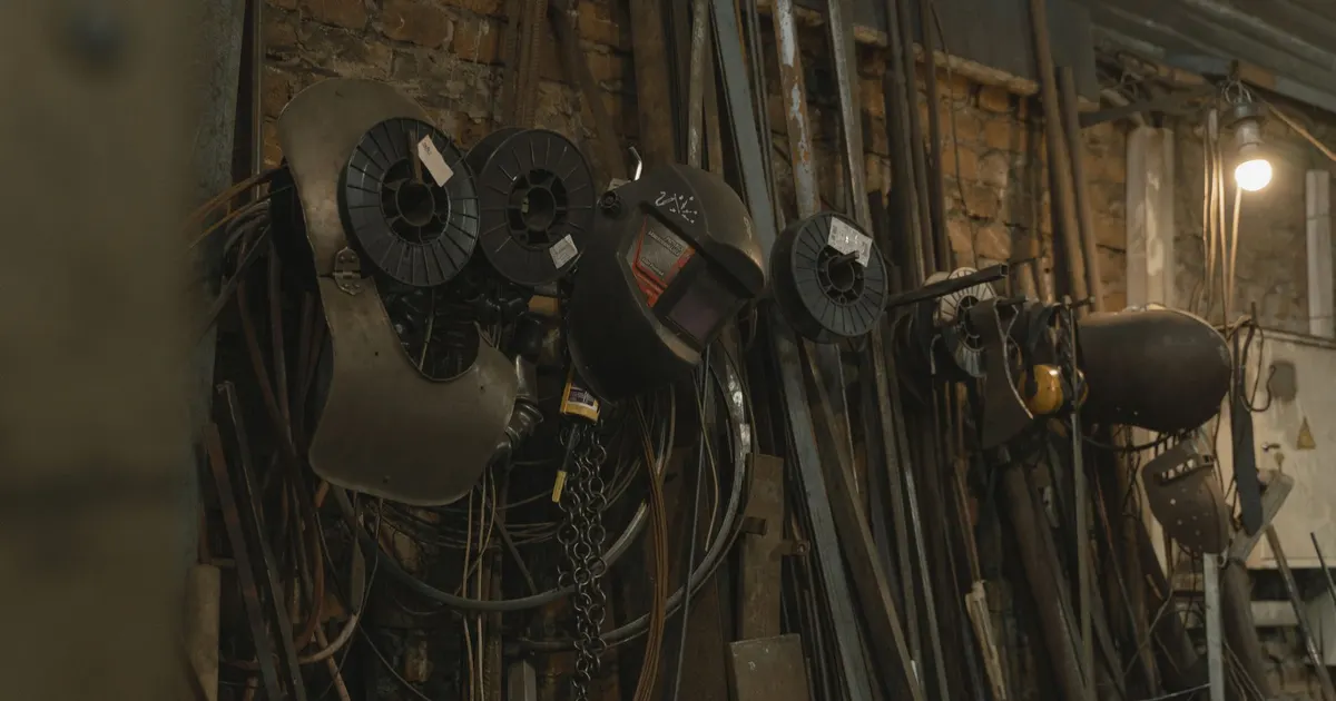 Spools of welding wire hanging on wire feeders in a fabrication workshop, the consumables selected for machine frame welding